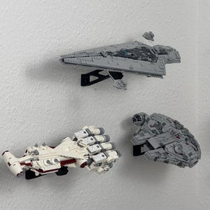 Può includere: Tre modelli di astronavi Lego Star Wars montati su una parete bianca. I modelli sono un'astronave bianca e rossa, un'astronave grigia e un'astronave grigia e rossa.