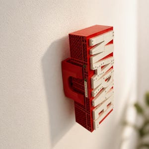 May include: A red and white LEGO-style sign spelling "MARVEL" mounted on a white wall. The sign is constructed from red and white interlocking bricks, with the letters in white. The sign has a unique, three-dimensional design.