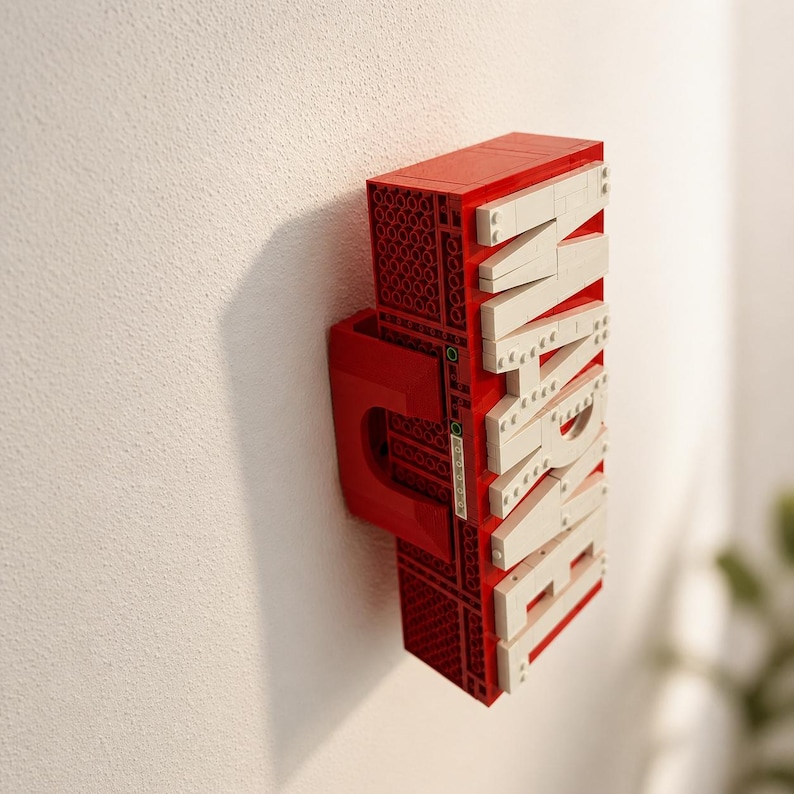 May include: A red and white LEGO-style sign spelling "MARVEL" mounted on a white wall. The sign is constructed from red and white interlocking bricks, with the letters in white. The sign has a unique, three-dimensional design.