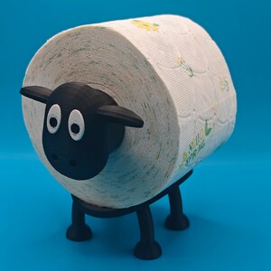 May include: A black sheep-shaped toilet paper holder with a white toilet paper roll with a floral pattern. The toilet paper roll is partially visible.