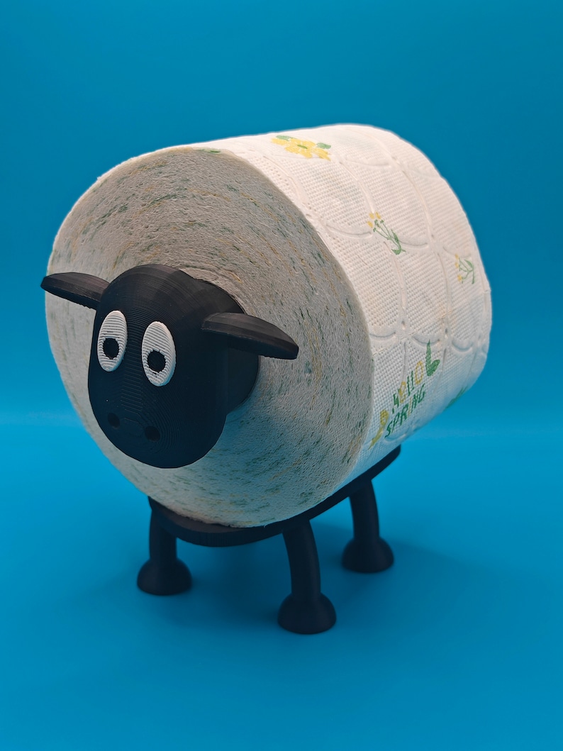 May include: A black sheep-shaped toilet paper holder with a white toilet paper roll with a floral pattern. The toilet paper roll is partially visible.