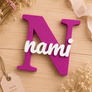May include: A large, magenta-colored capital letter N with the name nami written in white, lowercase, cursive script letters across the center. The letter N has a flat, matte finish and a thick, block-style font, while the name is layered on top.