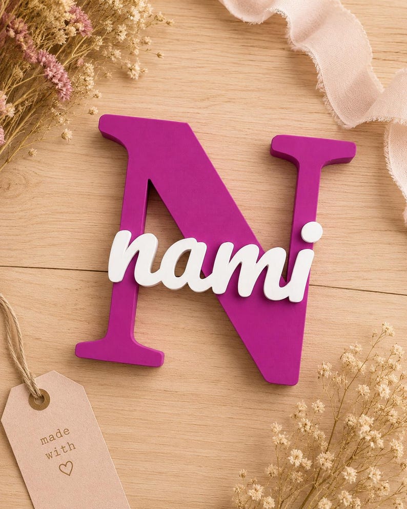 May include: A large, magenta-colored capital letter N with the name nami written in white, lowercase, cursive script letters across the center. The letter N has a flat, matte finish and a thick, block-style font, while the name is layered on top.