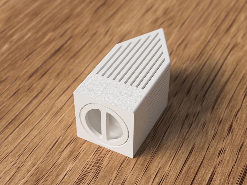 May include: A white, geometric object with a rectangular base and a slanted top featuring parallel lines. The front of the object has a circular design with a vertical divider. The object is set on a wooden surface.