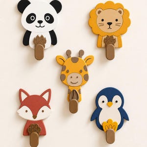 May include: A set of five animal-shaped wall hooks featuring a panda, lion, giraffe, fox, and penguin. Each hook displays a colorful character face with a brown, rectangular hook extending from the bottom, designed for hanging small items.