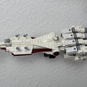 May include: A white and red model spaceship made from toy bricks. The model has multiple engines, a central body, and various details. The toy is designed to resemble a spacecraft.