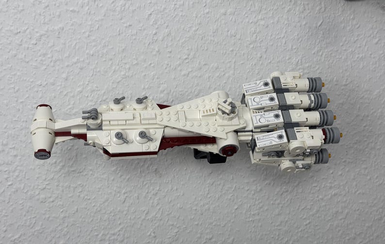 May include: A white and red model spaceship made from toy bricks. The model has multiple engines, a central body, and various details. The toy is designed to resemble a spacecraft.