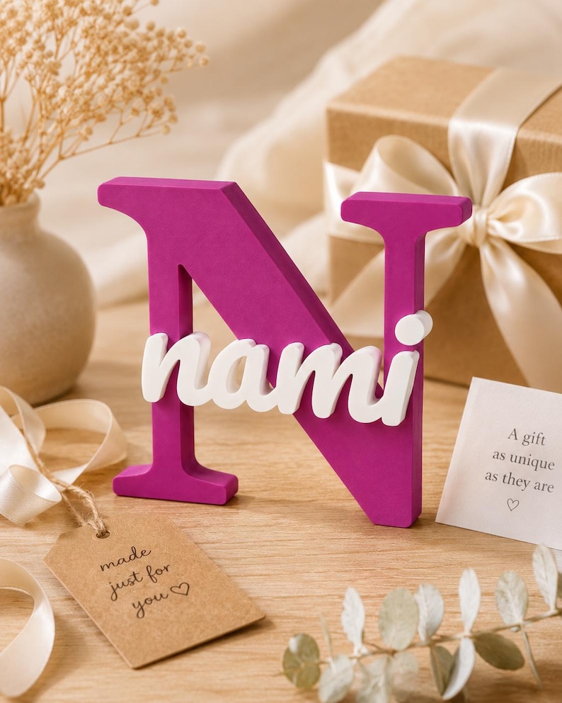 May include: A magenta-colored capital letter N with the white lowercase name nami attached to the front. The letter stands upright and features a smooth, matte finish. The name is written in a rounded, sans-serif font across the center of the letter.