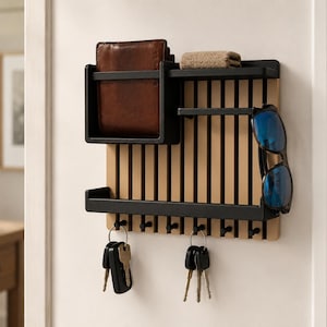 May include: A wall-mounted organizer featuring a light wood slatted back panel with black metal shelves and hooks. The unit holds a brown leather wallet, a small tan cloth, a pair of blue-tinted sunglasses, and two sets of metal keys on rings.