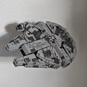 May include: A detailed model of the Millennium Falcon spaceship, constructed from interlocking building blocks. The model features a grey colour scheme with intricate detailing, including various panels, turrets, and circular elements. The spaceship is a popular item from the Star Wars franchise.