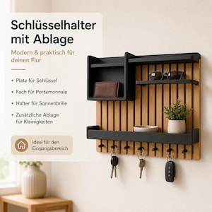 May include: A wall-mounted organizer featuring a light wood slat back panel with black metal shelves and hooks. The unit includes a box-style shelf, two narrow horizontal shelves, and a bottom tray. Three sets of keys hang from the black hooks.