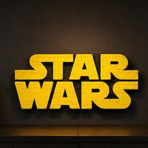 Pode incluir: Uma cole&ccedil;&atilde;o de capacetes de personagens de Star Wars, incluindo Darth Vader e Boba Fett, exibidos em uma prateleira. O logotipo amarelo "STAR WARS" est&aacute; centralizado acima dos capacetes. Cada capacete &eacute; uma r&eacute;plica detalhada, mostrando os designs ic&ocirc;nicos da franquia Star Wars.