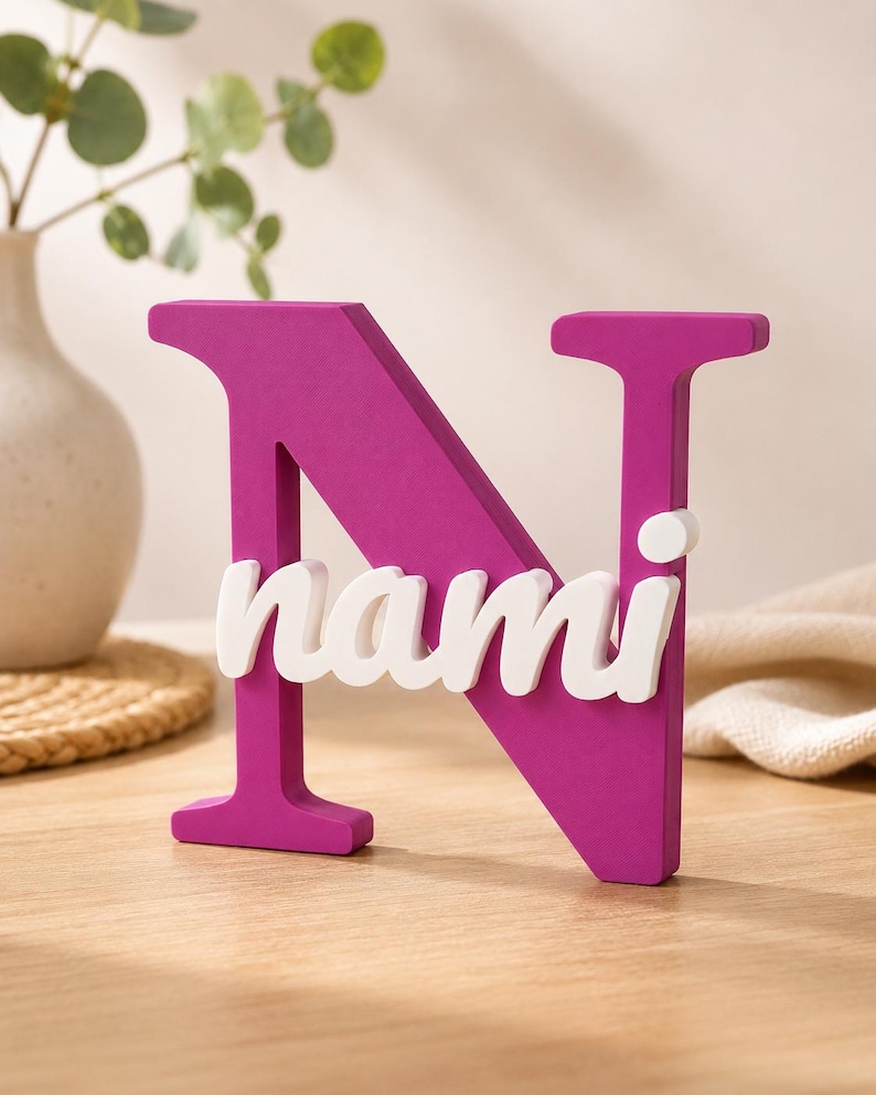 May include: A large, magenta-colored capital letter N made of a solid material. The white, lowercase name "nami" is attached horizontally across the center of the letter N. The object stands upright on a flat surface, displaying a smooth finish.