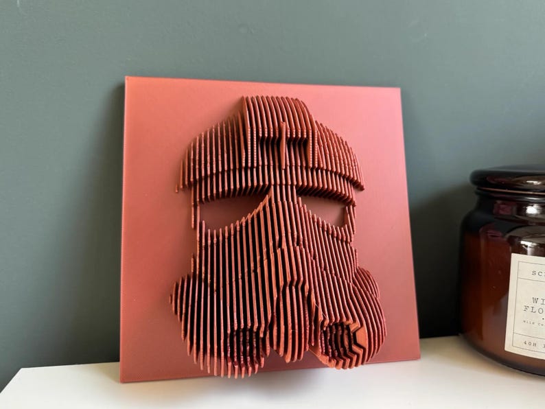 Puede incluir: Una pieza de arte de pared de madera roja que representa una cara estilizada con un casco. El casco est&aacute; hecho de muchas tiras de madera delgadas y verticales.