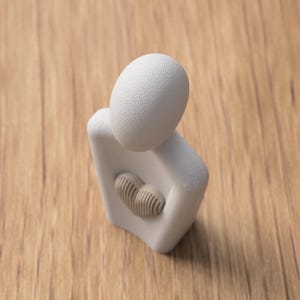 May include: A minimalist white ceramic sculpture of a person embracing a heart. The sculpture has a textured egg-shaped head and a heart-shaped cutout filled with a textured, tan-colored heart.