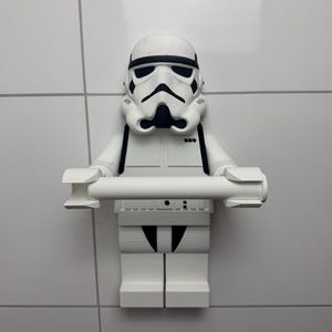 May include: White plastic Star Wars Stormtrooper figurine toilet roll holder. The figurine is holding a roll of toilet paper in its hands.