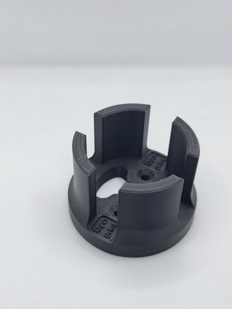 May include: A black, 3D-printed object with a circular base and four curved, vertical supports. The supports are evenly spaced around the circumference. The object has the text "layer print" on the side.