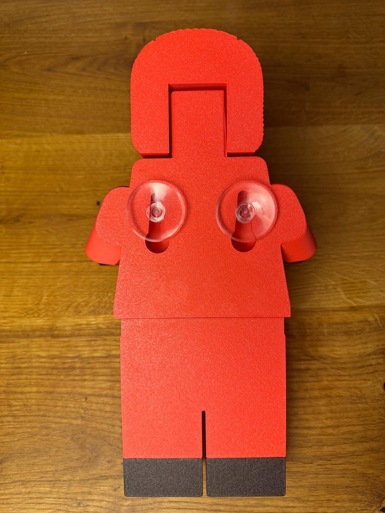 May include: Red foam figurine of a person with suction cups on the back. The figurine is shaped like a Lego person.