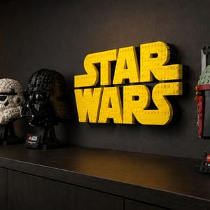 Pode incluir: Uma exibi&ccedil;&atilde;o de capacetes LEGO Star Wars e um letreiro amarelo "STAR WARS". Os capacetes incluem um Stormtrooper branco, um Darth Vader preto, um capacete de piloto vermelho e branco e um capacete Boba Fett verde e vermelho. O letreiro &eacute; feito de tijolos LEGO amarelos.