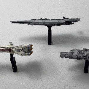 May include: Three Star Wars spaceship models, including the Millennium Falcon, a Star Destroyer, and a smaller ship, are displayed on black stands against a white wall. The models are detailed and grey.
