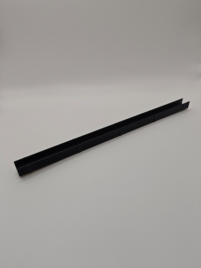 May include: A long, black, U-shaped metal channel. The channel is rectangular with a flat base and two parallel sides. The object is set against a plain white background.