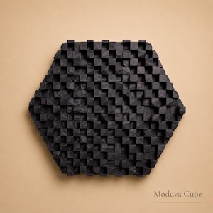 May include: A black, hexagonal wall art piece with a textured surface made of small, square wooden blocks. The artwork, labeled "Moduva Cube," is set against a neutral background, creating a striking contrast. The design is modern and geometric.