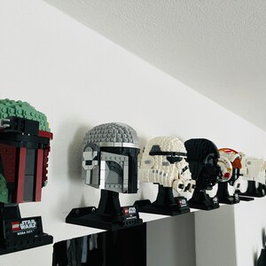 Puede incluir: Una colecci&oacute;n de ocho modelos de cascos LEGO Star Wars expuestos en un estante. Los cascos son todos de diferentes colores y dise&ntilde;os, incluyendo Boba Fett, Darth Vader y un Stormtrooper.