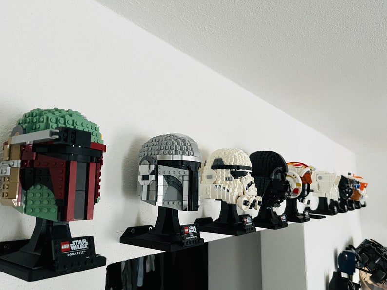 Puede incluir: Una colecci&oacute;n de ocho modelos de cascos LEGO Star Wars expuestos en un estante. Los cascos son todos de diferentes colores y dise&ntilde;os, incluyendo Boba Fett, Darth Vader y un Stormtrooper.