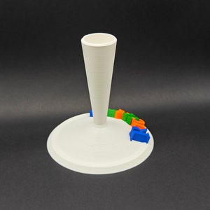 Puede incluir: Soporte blanco impreso en 3D con una parte superior en forma de cono y una base circular. El soporte tiene la palabra "GOOGLE" impresa en color alrededor de la base.