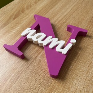 May include: A large, magenta-colored capital letter N with a smaller, white, cursive-style script overlay spelling the name nami. The letters are three-dimensional with a flat front surface and thick, solid sides, creating a layered appearance.