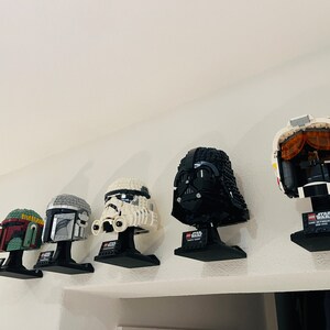 Puede incluir: Una colecci&oacute;n de cinco cascos LEGO de Star Wars en exhibici&oacute;n. Los cascos son de Darth Vader, Boba Fett, un Stormtrooper, un piloto de caza TIE y un Mandaloriano. Cada casco est&aacute; montado en un soporte negro con el logotipo de Star Wars.