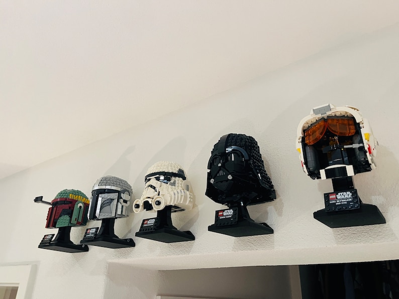 Puede incluir: Una colecci&oacute;n de cinco cascos LEGO de Star Wars en exhibici&oacute;n. Los cascos son de Darth Vader, Boba Fett, un Stormtrooper, un piloto de caza TIE y un Mandaloriano. Cada casco est&aacute; montado en un soporte negro con el logotipo de Star Wars.
