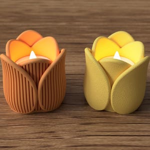 May include: Two tulip-shaped candle holders. One is orange with vertical lines, the other is yellow with a textured surface. Each holds a lit white candle, creating a warm glow. The candle holders sit on a wooden surface.