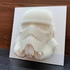 Puede incluir: Arte de pared impreso en 3D blanco de un casco de Stormtrooper de Star Wars. El casco est&aacute; hecho de l&iacute;neas delgadas y superpuestas que crean un aspecto &uacute;nico y moderno.