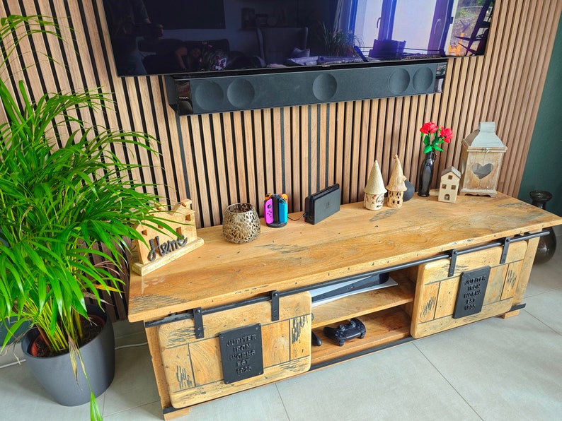 May include: A reclaimed wood TV unit with sliding doors and metal detailing. The unit has a natural wood finish and is adorned with decorative items, including a plant, ornaments, and gaming consoles. The unit is approximately 150 cm long.