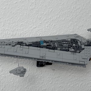 May include: A grey Lego model of a Star Destroyer spaceship, mounted on a white wall. The model is detailed with various grey blocks and features two smaller Lego ships. The model is approximately 61 cm long.