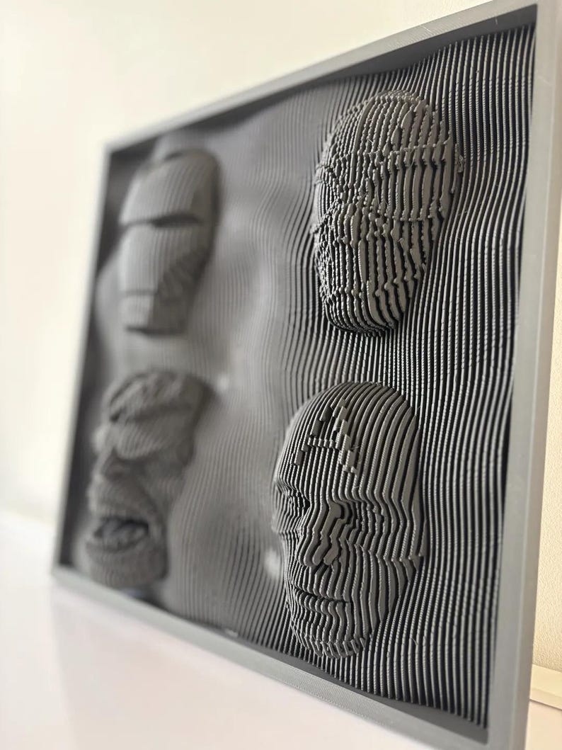 May include: A gray framed wall art piece with three 3D faces created using a layered, striped design.