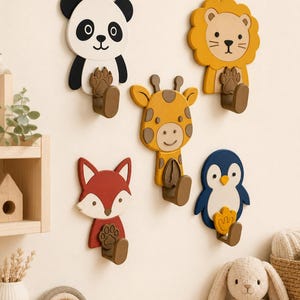 May include: A set of five wall-mounted animal hooks featuring a panda, lion, giraffe, fox, and penguin. Each hook is shaped like an animal face with a corresponding paw or foot print design on the brown hook base, providing functional storage.