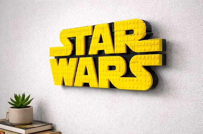 Pode incluir: Um logotipo "STAR WARS" amarelo e preto feito de blocos interligados, montado em uma parede branca. As letras s&atilde;o amarelas e o fundo &eacute; preto. Uma pequena planta em vaso est&aacute; localizada abaixo do logotipo.