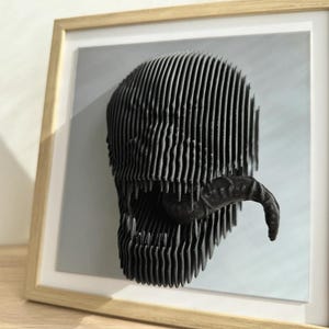 May include: A black and white 3D printed sculpture of a Venom character's head, displayed in a wooden frame.