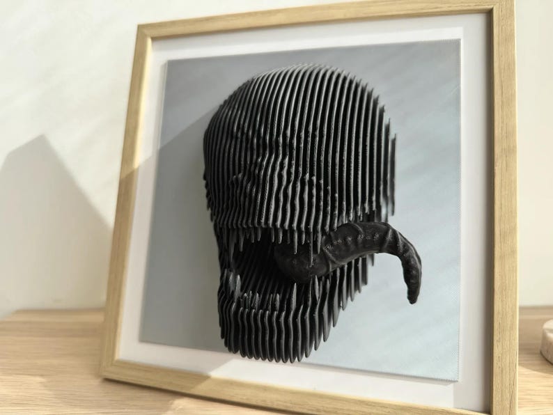 May include: A black and white 3D printed sculpture of a Venom character's head, displayed in a wooden frame.