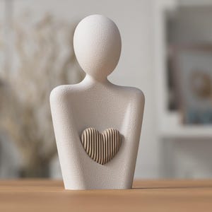 May include: A cream-colored sculpture of a person holding a heart. The figure has a smooth, textured surface. The heart is made of vertical wooden slats. The sculpture is a decorative item.