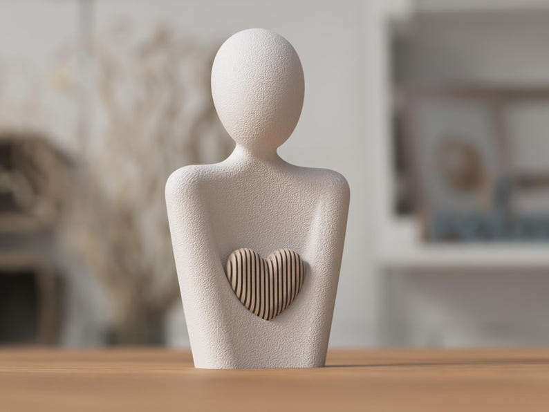 May include: A cream-colored sculpture of a person holding a heart. The figure has a smooth, textured surface. The heart is made of vertical wooden slats. The sculpture is a decorative item.