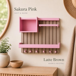 Op de afbeelding: Een wandorganizer met een verticaal lattenontwerp in lattebruin met sakura-roze accenten. Het bevat een vierkante opbergdoos, twee horizontale planken en zes kleine haken aan de onderkant. De tekst Sakura Pink en Latte Brown is zichtbaar.
