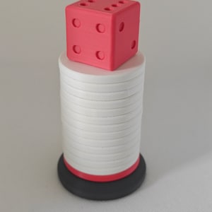 May include: A red dice sits on top of a stack of white circular pieces. The stack is on a black base with a red ring.