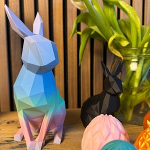 May include: A set of colorful geometric Easter decorations, including a blue, green, and pink bunny, a black bunny, and pink and teal eggs.