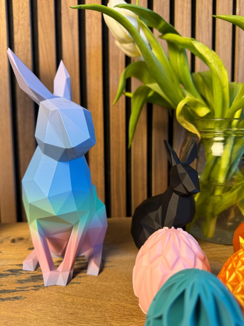 May include: A set of colorful geometric Easter decorations, including a blue, green, and pink bunny, a black bunny, and pink and teal eggs.