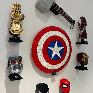 Puede incluir: Una colecci&oacute;n de construcciones Lego de personajes de Marvel montadas en una pared blanca. Incluye un Guantelete del Infinito dorado, el martillo de Thor, el escudo del Capit&aacute;n Am&eacute;rica, el casco de Iron Man y otros bustos de personajes.