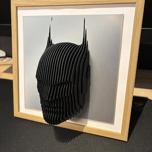 May include: A black and white 3D printed Batman head sculpture in a wooden frame with a gray mat.