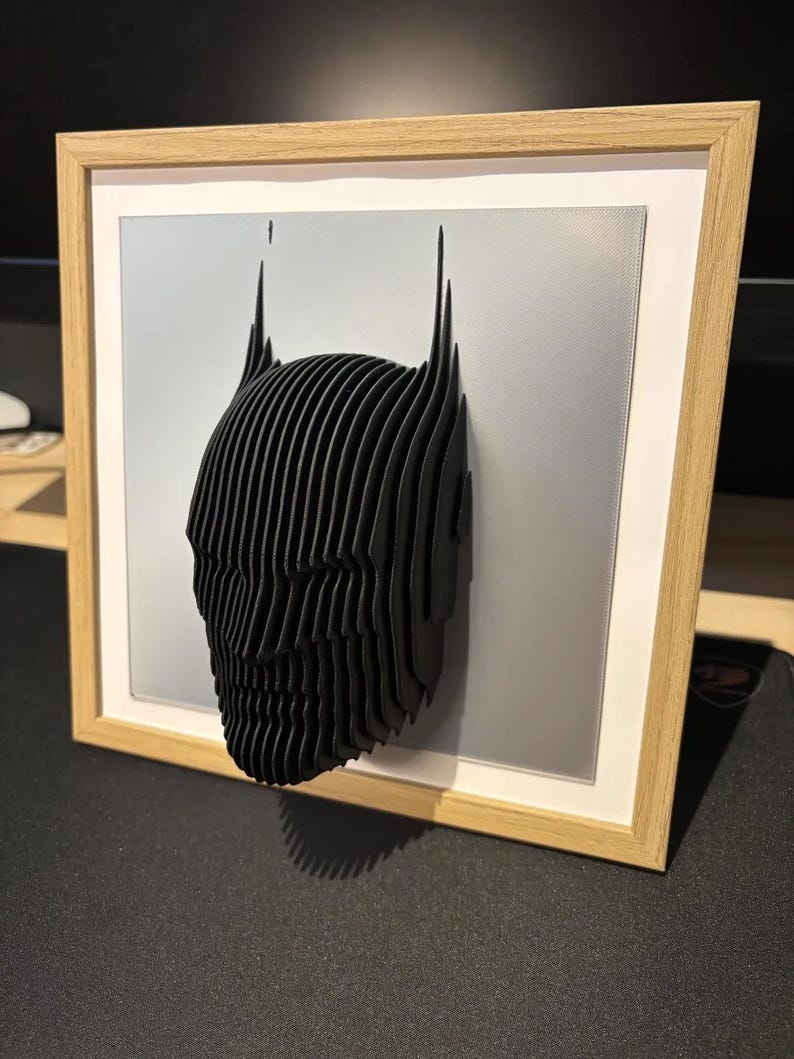 May include: A black and white 3D printed Batman head sculpture in a wooden frame with a gray mat.